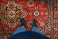 Man stands on the carpet and takes a photo of his feet. Fashionable sneakers on her feet and wears jeans. Background. Photo of Royalty Free Stock Photo