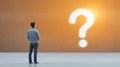 man stands in front of large glowing question mark on textured wall symbolizing curiosity and contemplation warm light creates Royalty Free Stock Photo