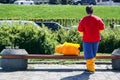 A man stands with his back in a costume of Bart Simpson, whose head lies next to the bench