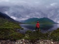 Man stands by lake in red jacket in cloudy weather panorama Royalty Free Stock Photo