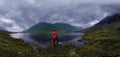 Man stands by lake in red jacket in cloudy weather panorama Royalty Free Stock Photo