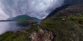 Man stands by lake in red jacket in cloudy weather panorama Royalty Free Stock Photo