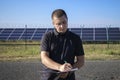 A man stands near a solar power plant with a notebook and a pen in his hands. A technician checks the functionality of solar