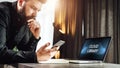 Man stands near table with laptop with inscription on monitor- cloud library, looks at screen of smartphone. Online education