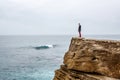 Man stands on a sea cliff, looking into the distance on a dark stormy sea.