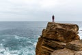 Man stands on a sea cliff, looking into the distance on a dark stormy sea.