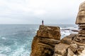 Man stands on a sea cliff, looking into the distance on a dark stormy sea.