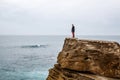 Man stands on a sea cliff, looking into the distance on a dark stormy sea.