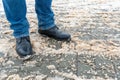 A man stands on the sidewalk in snow and mud. Black shoes and blue jeans close-up on the background of dirty snow. Ice on the road Royalty Free Stock Photo