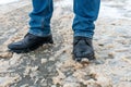 A man stands on the sidewalk in snow and mud. Black shoes and blue jeans close-up on the background of dirty snow. Ice on the road Royalty Free Stock Photo