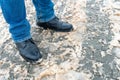 A man stands on the sidewalk in snow and mud. Black shoes and blue jeans close-up on the background of dirty snow. Ice on the road Royalty Free Stock Photo