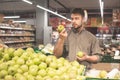 Man stands in a supermarket, holds apples in his hands, buyer wears a shirt buying apples. Man with a beard chooses apples in the