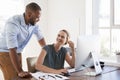Man stands talking to woman smiling at her desk in an office Royalty Free Stock Photo