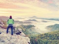 Man stay on rocky peak within daybreak and watch over misty landscape.