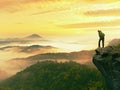 Man stay on rocky peak within daybreak and watch over misty landscape.