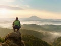 Man stay on rocky peak within daybreak and watch over misty landscape.