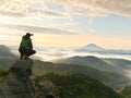 Man stay on rocky peak within daybreak and watch over misty landscape.