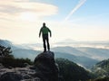 Man stay on rocky peak within daybreak and watch over misty landscape.