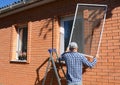 A man on a step ladder is installing a mosquito net, fly screen or frame on plastic window  to prevent different insects, bugs Royalty Free Stock Photo