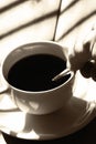 Man stiring a cup of black coffee in sunlight on a wooden table