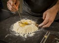 A a man stirring eggs into a mound of flour with a fork