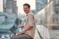 Man on the street. Attractive man sitting outside, using mobile phone and laptop, smiling Royalty Free Stock Photo