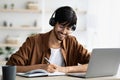 Man Studying at Home With Headphones While Writing Notes in a Notebook and Using a Laptop in a Well-Lit Room Royalty Free Stock Photo