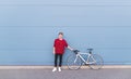 Man in stylish clothes is standing with a white bicycle on the background of a blue wall and looking at the camera Royalty Free Stock Photo