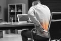 Man suffering from back pain while working with laptop in office. Symptom of poor posture Royalty Free Stock Photo