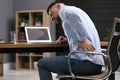 Man suffering from back pain while working with laptop in office. Symptom of poor posture Royalty Free Stock Photo