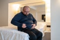 Man suffering from extra weight touching abdomen sitting on bed in bedroom.