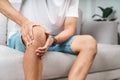 The man suffering from knee pain sitting on the couch hold and massaging his painful knee Royalty Free Stock Photo