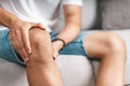 The man suffering from knee pain sitting on the couch holding and massaging his painful knee Royalty Free Stock Photo