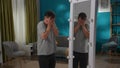 A man suffering from a mental disorder stands in front of a mirror, hiding his face in his hands. Apathy, inner conflict