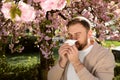 Man suffering from seasonal pollen allergy near blossoming tree outdoors Royalty Free Stock Photo