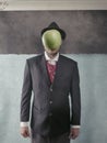 Man in a suit and hat standing near the wall with a green apple in front of his face Royalty Free Stock Photo