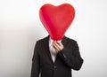 Man in suit hiding behind a red heart shaped balloon. Man holding symbol of love, family, hope Royalty Free Stock Photo