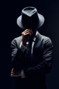 Man in suit hiding face behind his hat isolated on dark background