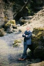 Man in a suit with his arms crossed on his chest stands leaning on a huge boulder