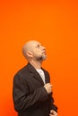 Man in suit jacket, bearded and bald looking up and making gestures