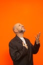 Man in suit jacket, bearded and bald looking up and making gestures