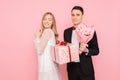 Man in a suit makes a surprise to a woman, gives a bouquet of flowers and a box with a gift, on a pink background Royalty Free Stock Photo