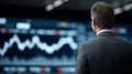 A man in a suit is observed from behind, looking at a large screen displaying a financial chart with fluctuating lines Royalty Free Stock Photo