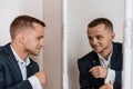 Man in a suit smiles at his reflection in the mirror. Perfect look