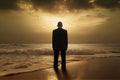 a man in a suit standing on a beach at sunset looking out to the ocean with waves coming in from the ocean and a cloudy sky Royalty Free Stock Photo
