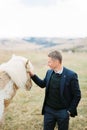 Man in a suit strokes a horse in a valley. Iceland