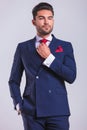 Man in suit in studio with hand in pocket while fixing his tie