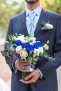 Man in suit and stylish tie is holding wedding bouquet