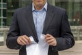 A man in a suit tearing a piece of paper against the background of a modern office building. Concept: termination of contract,