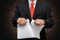 A man in a suit tears up a piece of paper against a brick wall. concept: termination of the contract, invalid document, dismissal